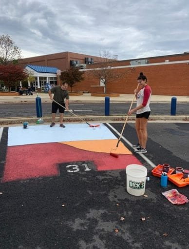 Students express creativity and start on the painting of a spot in front of the athletic entrance. A wide variety of colors pop against the black asphalt. Take a spin through the lot to see more of these works of art. Photo courtesy of Matthew Prince.