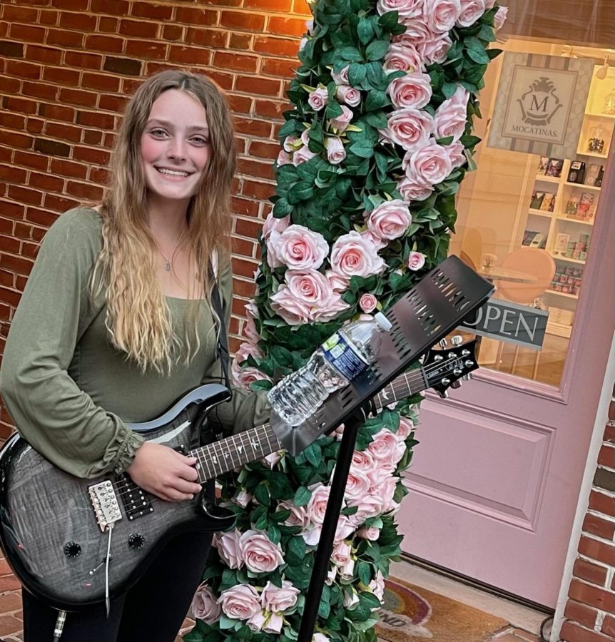 Olivia Dewan, a junior, poses with her guitar in front of Mocatinas, an ice cream parlor and bakery where she performs during First Fridays.