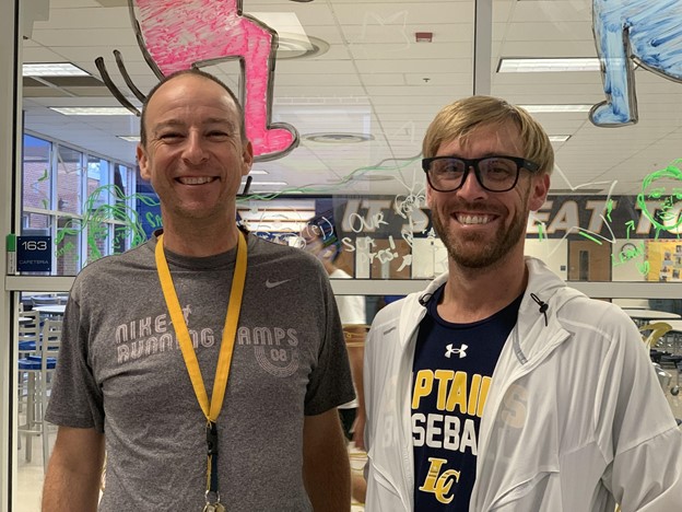 Coach Rudy and Coach Beck pose in front of the cafeteria while stretching before practice for the day. Rudy and Beck both joined the cross country team this year as assistant coaches.