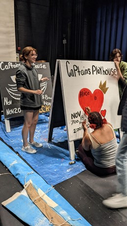 Kat Blackwood (left), Jada Venson (middle), and Maxwell McKnight, work backstage to create the advertisement signs for “Alice in Wonderland”