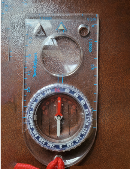 A standard orienteering compass. The clear body and magnifying glass makes reading maps easier. Surrounding the flat sides are measurement tools to help calculate scale on maps. 