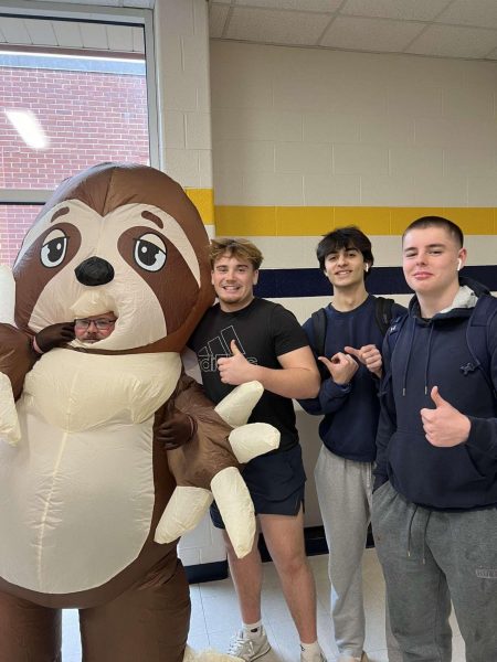 Dryden dresses in his sloth costume to visit students in their classroom. He posed for a picture with junior Chris Duellman (left), senior Eddie Azzouz (middle), and junior Ben Bilko (right). 