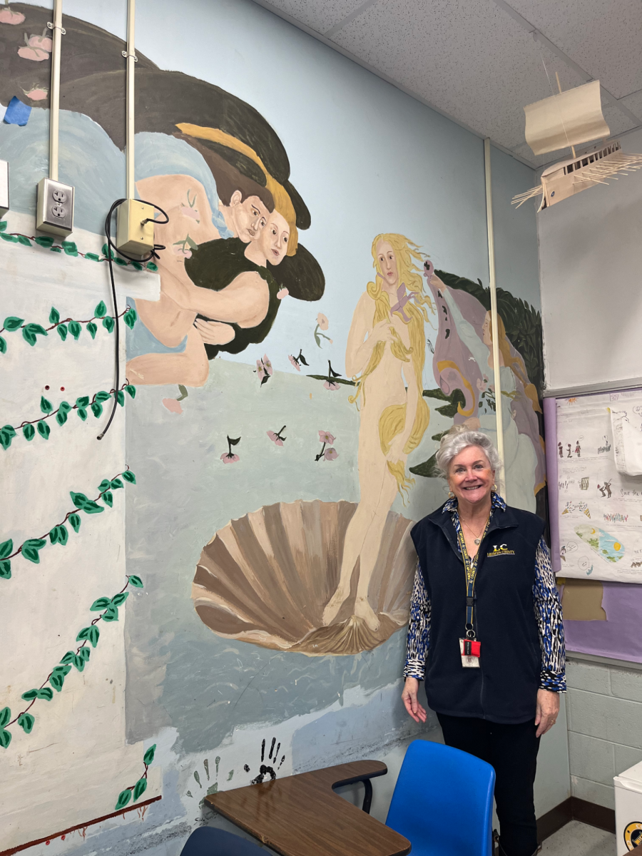 Lynn Krepich stands in front of the first mural painted in her classroom by a previous student in 1995. The mural depicts Sandro Botticelli “The Birth of Venus.”